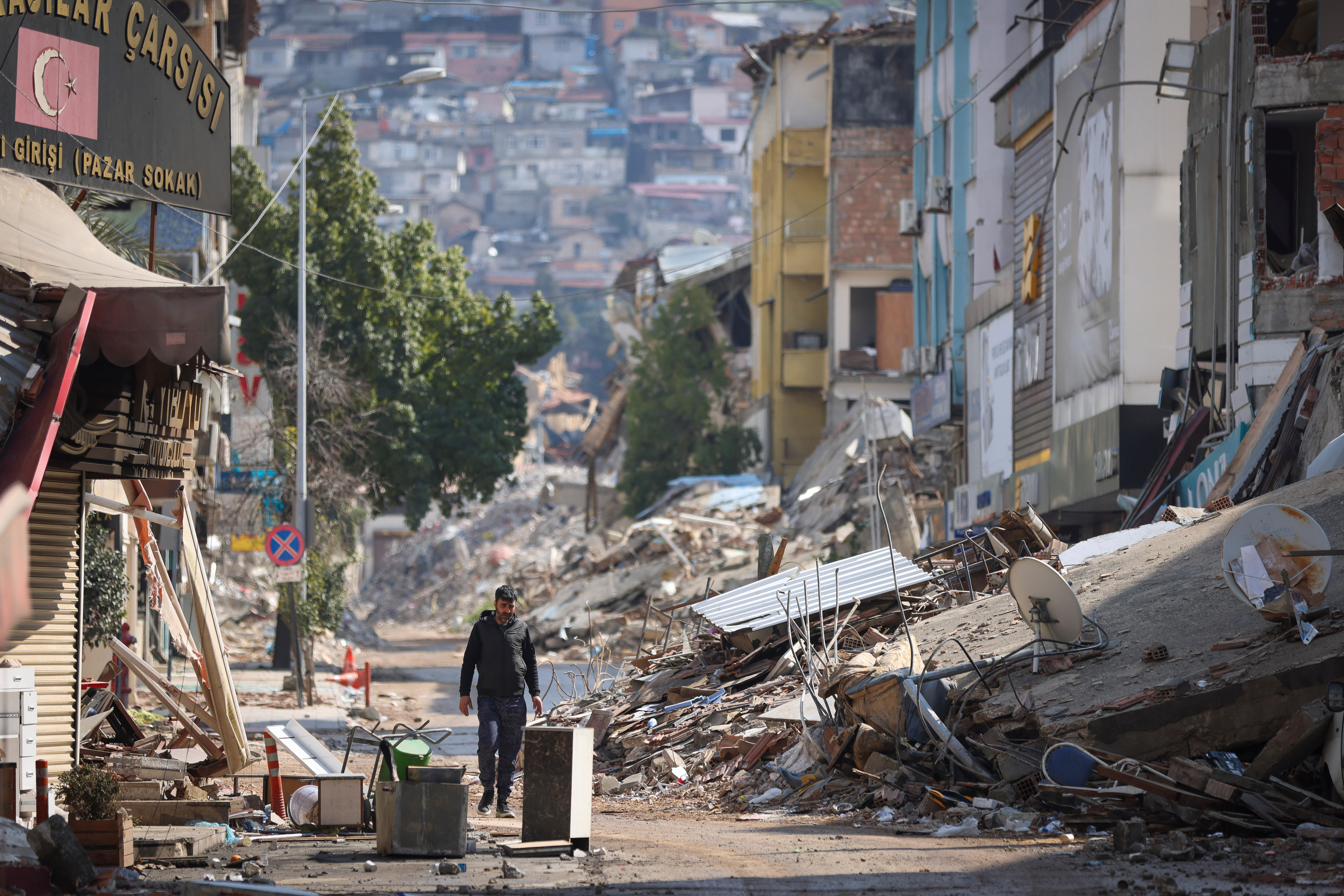 A man walks down a street surrounded by rubble.