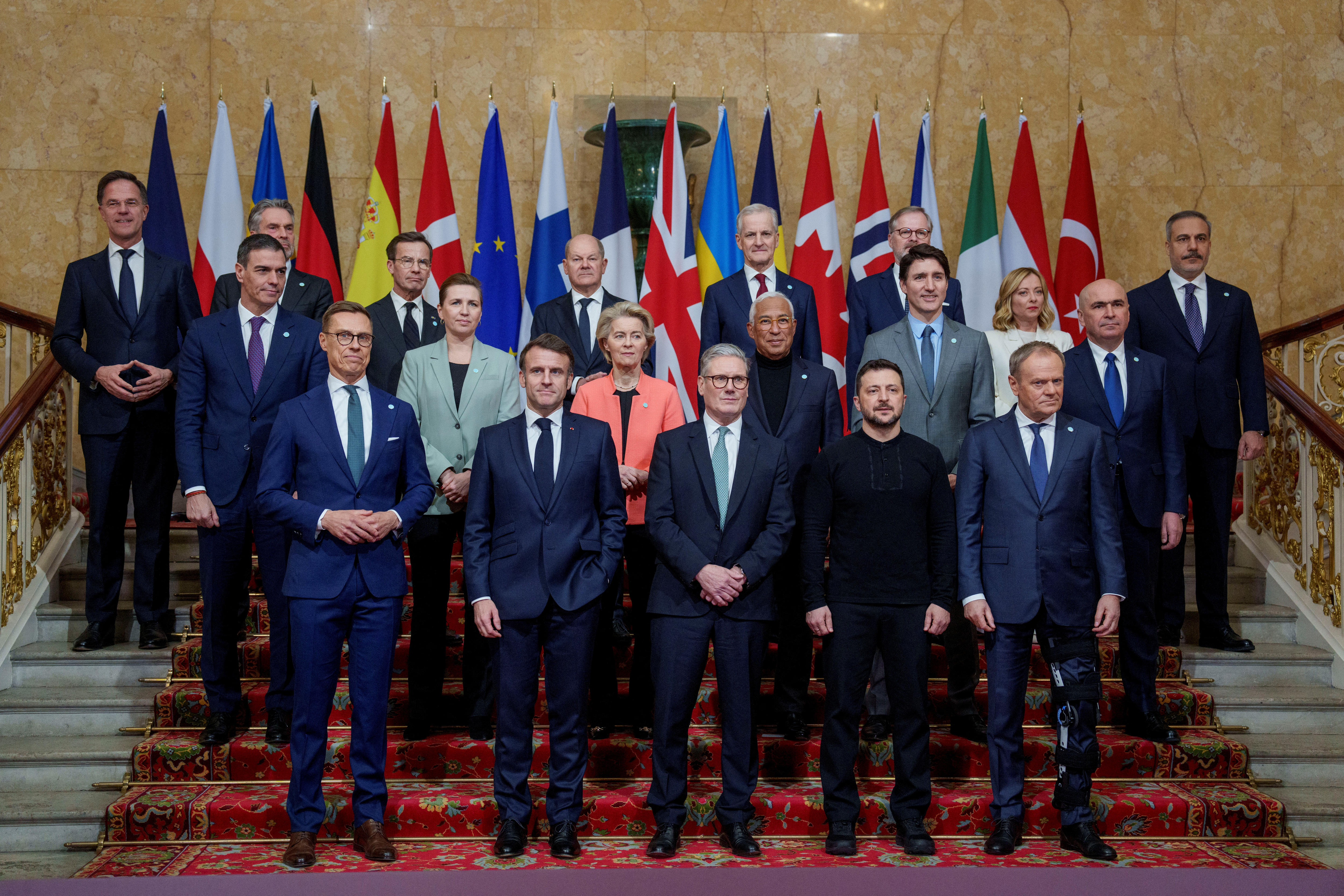 leaders of european countries stand for a group photo on stairs with their flags in a row behind