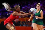 A Malawi netballer's hair flies behind her as she reaches out to grab the ball ahead of a Northern Ireland opponent.