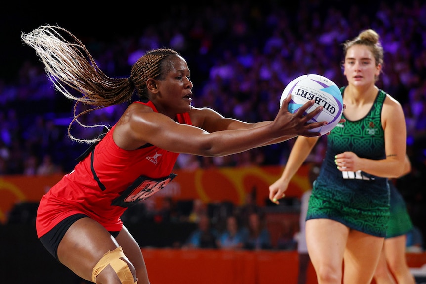 A Malawi netballer's hair flies behind her as she reaches out to grab the ball ahead of a Northern Ireland opponent.