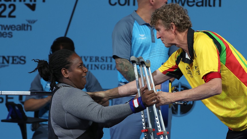 A woman wearing grey is handed crutches from a man wearing yellow