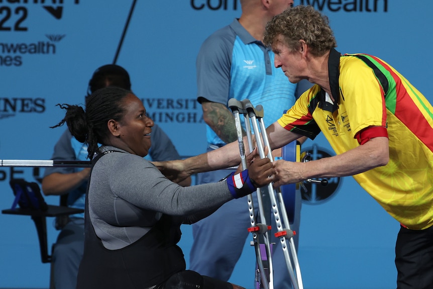 A woman wearing grey is handed crutches from a man wearing yellow
