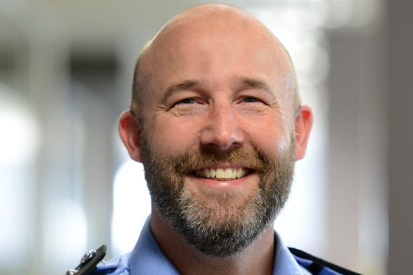 Middle aged man in a police uniform smiling.