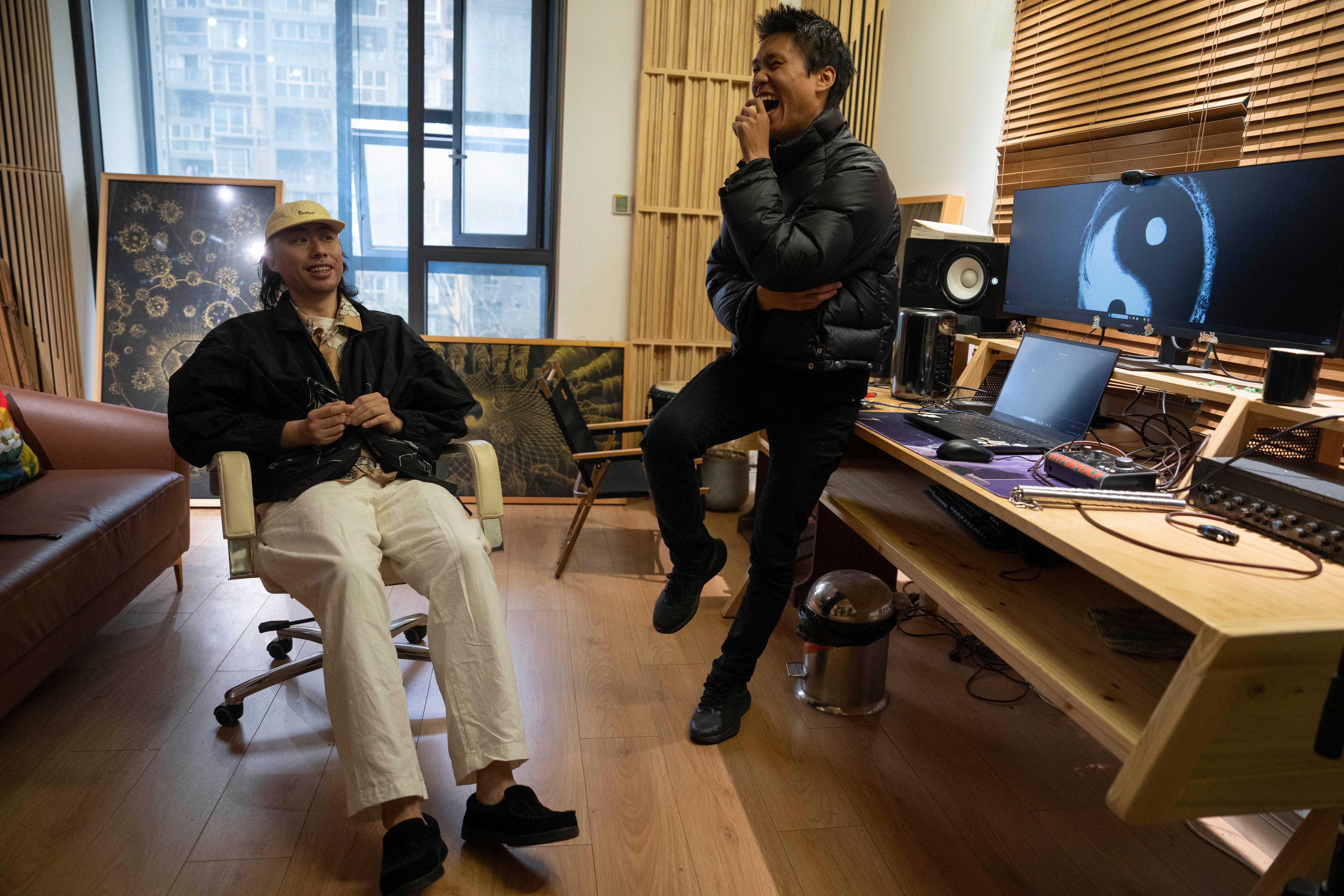 Two young Chinese men laugh in a room that contains some sound recording equipment.