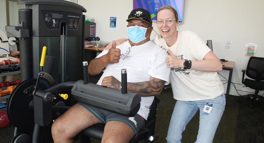 Johnnie Tumai en el gimnasio con su ayudante Julie Price, ambos con ropa de gimnasia. 