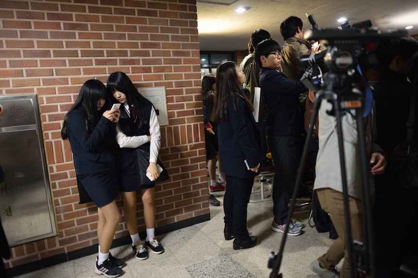 Two students read the news on a phone at the edge of a press conference at Danwon High School.