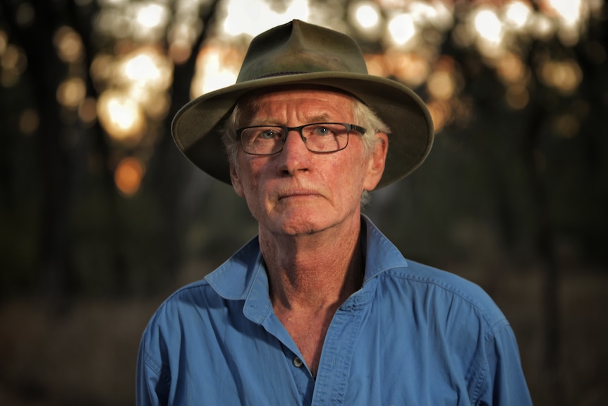 A man wearing a blue collared shirt and broad rimmed hat.