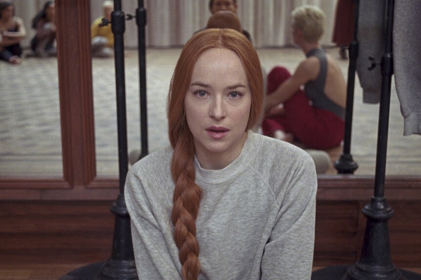 Colour still of Dakota Johnson in a dance rehearsal room, looking to camera in 2018 film Suspiria.