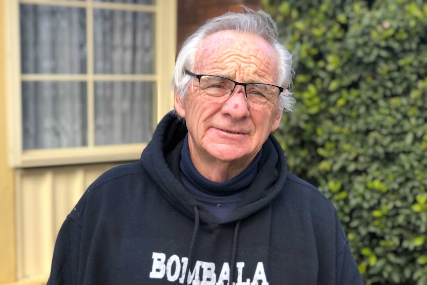 An older man with white hair, glasses, and a jumper.