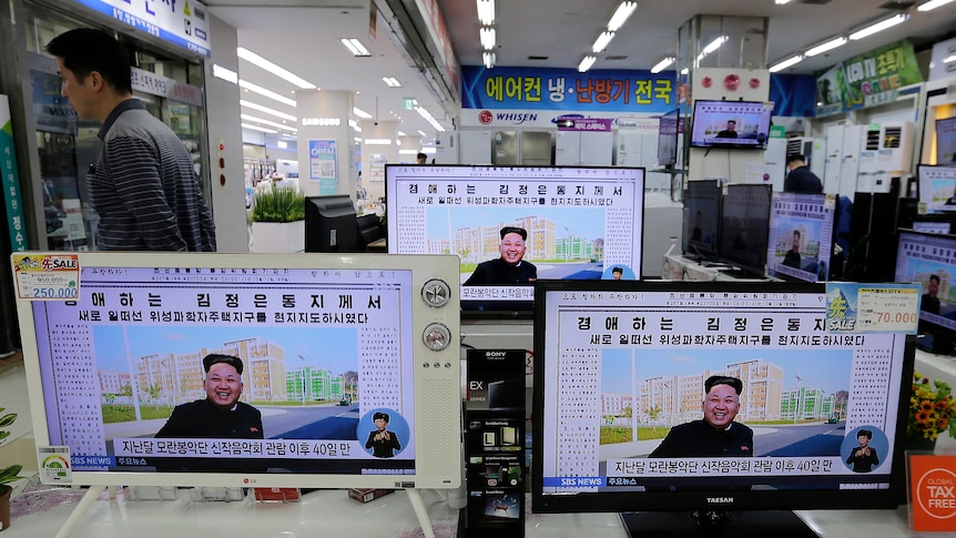 Three monitors showing a North Korean newspaper article with a photo of North Korean leader Kim Jong Un.