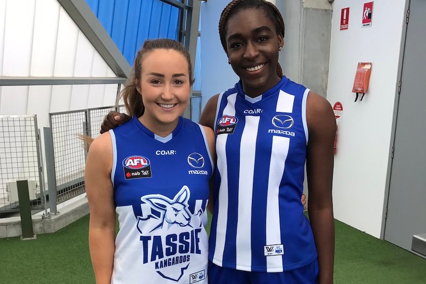 AFLW players Nicole Bresnehan and Loveth Ochayi wearing the North Melbourne and Tassie home guernseys.