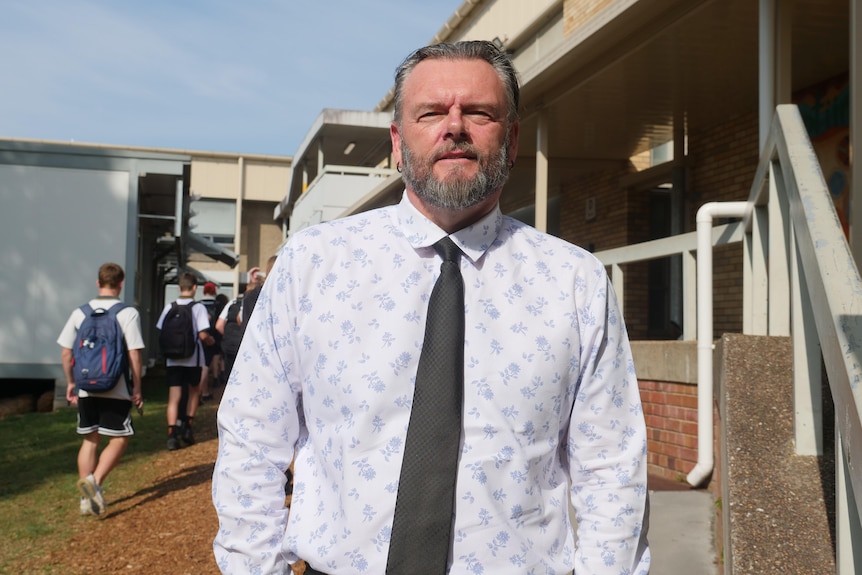 the principal of a high school, a man, stands in front of classrooms and looks at the camera