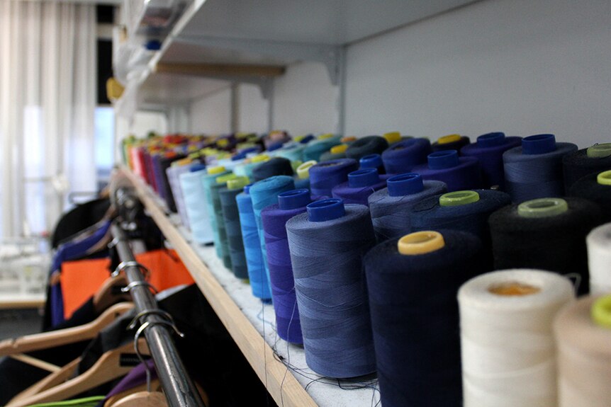 Spools of coloured thread on a shelf in a clothing alteration workshop.