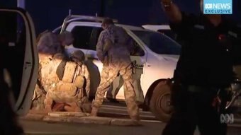 Three officials crouch over suspected gunman in Darwin. They wear camouflage gear and a white ute is behind them.