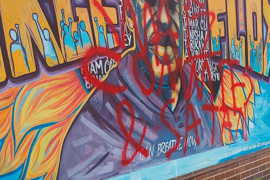 Mural dedicated to George Floyd has writing in spray painted in red over the picture.