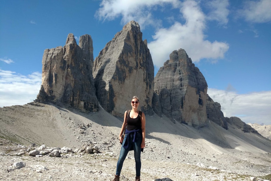 A young woman in hiking gear poses in front of some desert mountains.