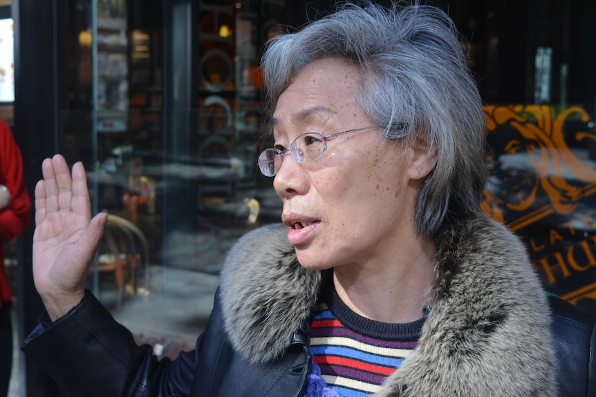 A woman with short grey hair gestures as she speaks to a reporter.