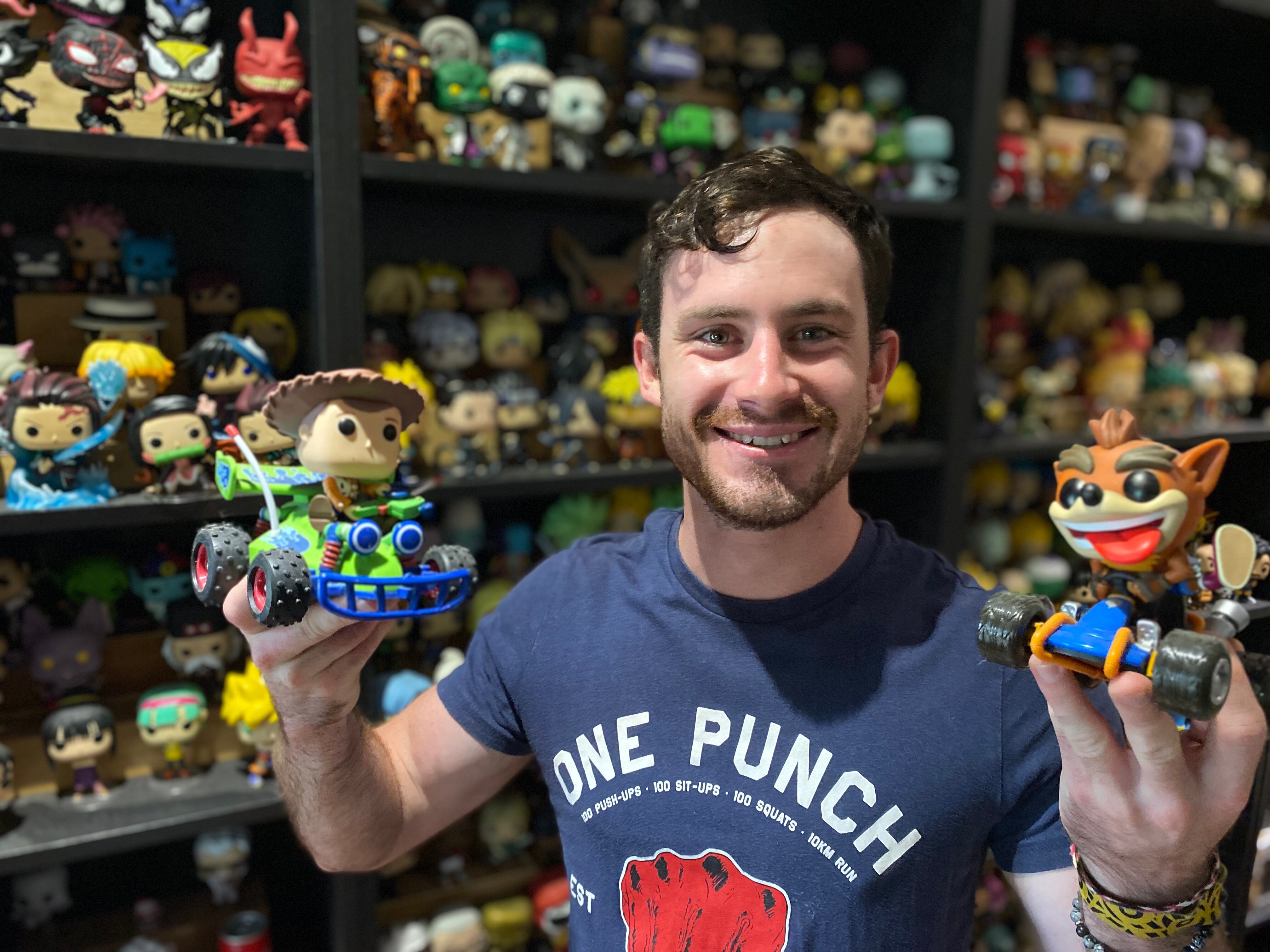 smiling man holds up a toy story and crash bandicoot pop vinyl figurine 