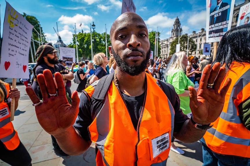 An anti-knife protester wearing an orange hi-vis vest holds his arms up towards the camera