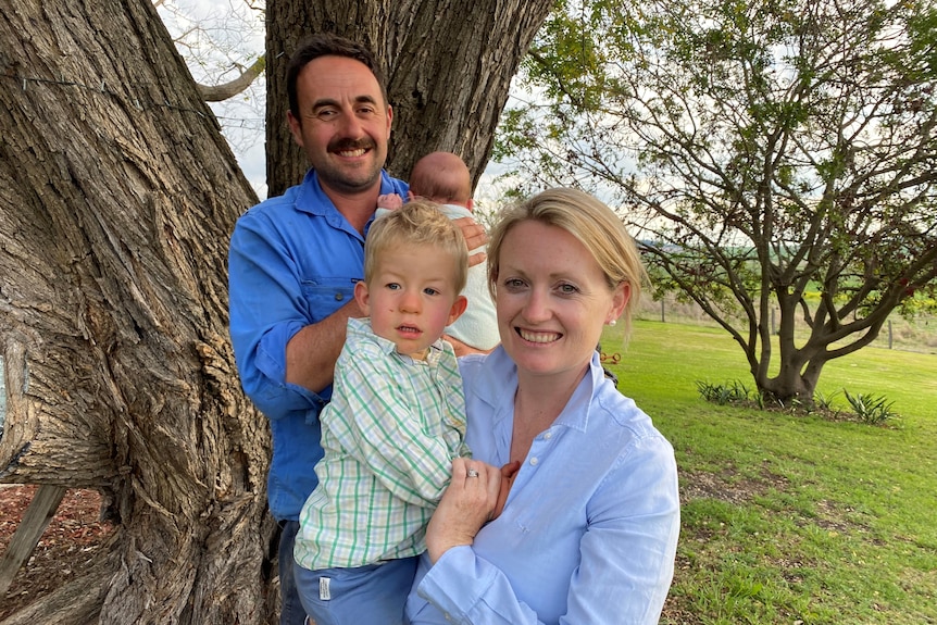 A family smiling at the camera with a father holding a baby and a mother holding a toddler