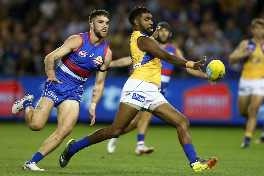 A West Coast Eagles AFL player drops the ball from his right hand as he prepares to kick.