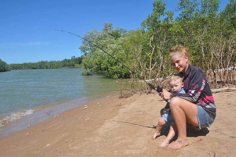 Fisherwoman fishing from shore with her young son.