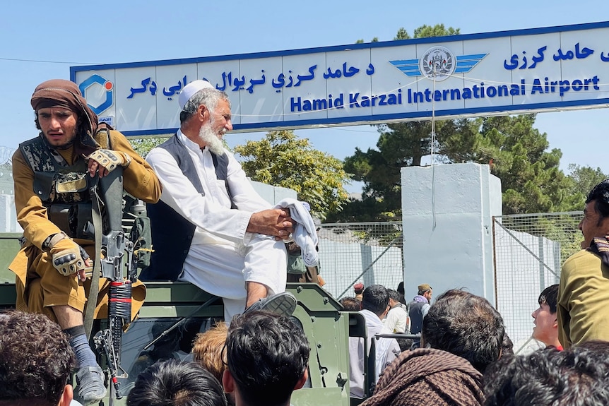 Two men sit on an armored car in front of Hamid Karzai Airport