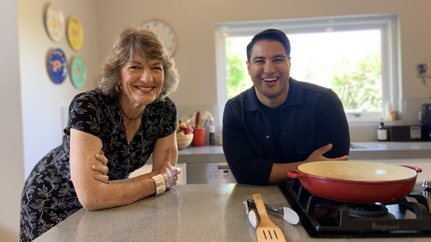 A woman in a dark dress and a man in a navy shirt pose for a photo in a home kitchen