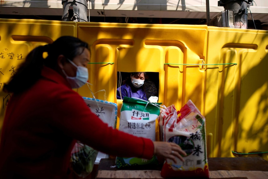 A woman wears a face mask to buy food through a yellow barrier in Wuhan.