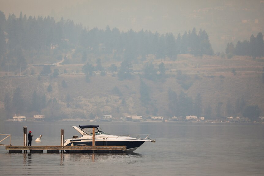 A boat sit on the lake surrounded by smoke in the background.