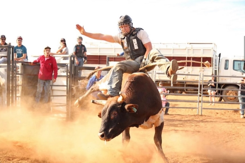 Teenage boy riding a bull at a dusty rodeo ground 
