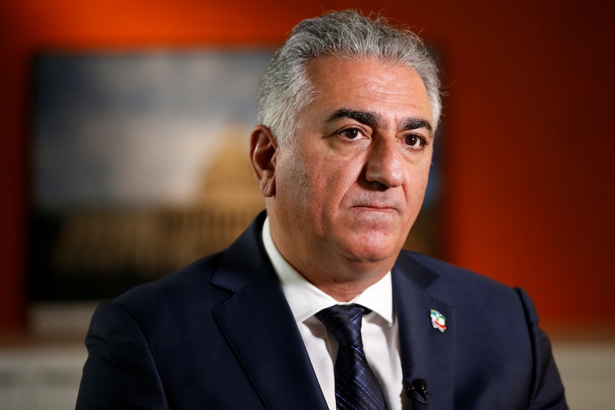 Reza Pahlavi, a man wearing a navy suit with a tiny pin depicting the Iranian flag