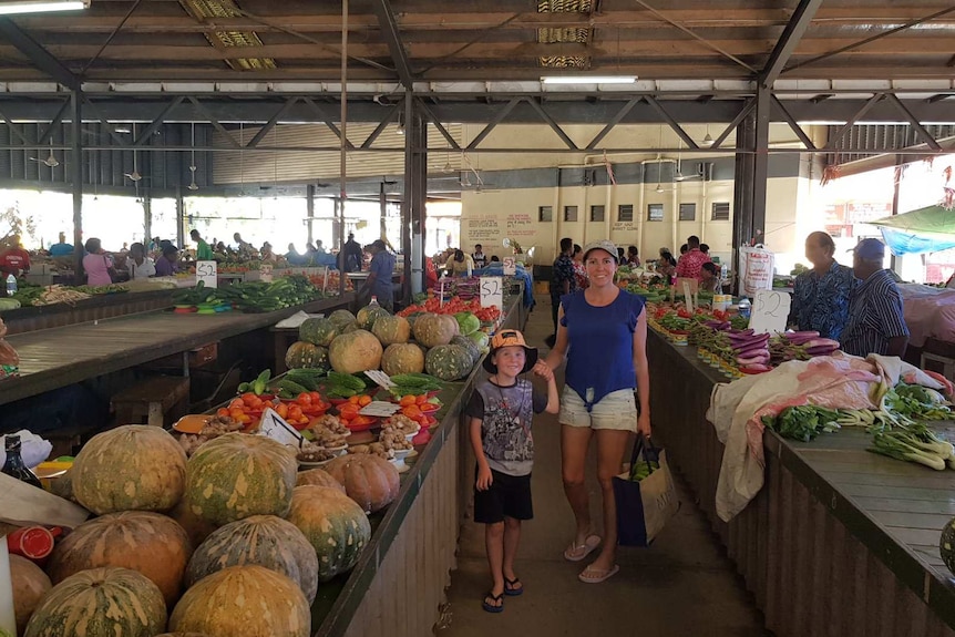 a woman and young boy stand in the aisle of a warehouse next to a table full of fresh vegetables