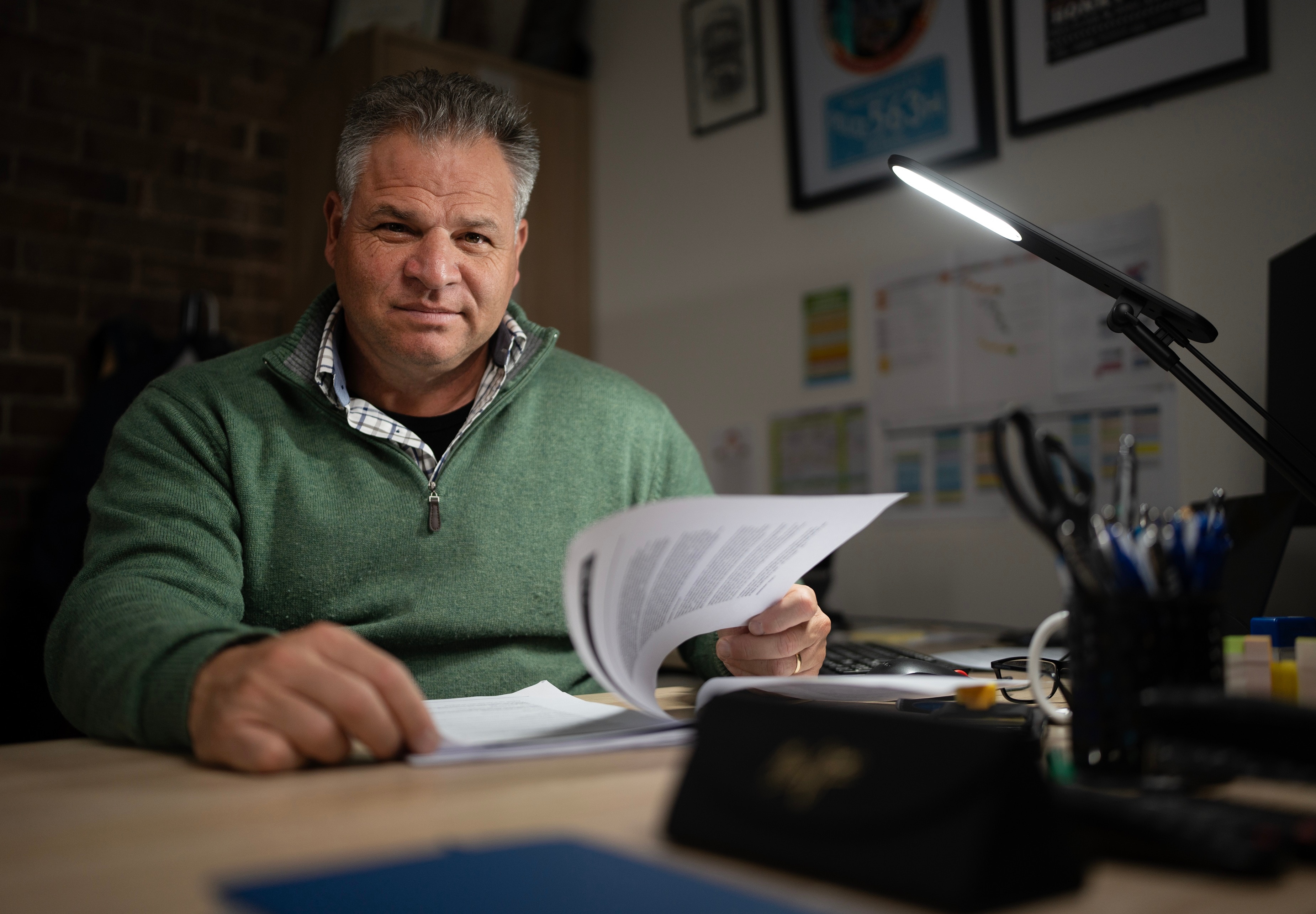 Man sitting at desk, holding a document, staring at camera