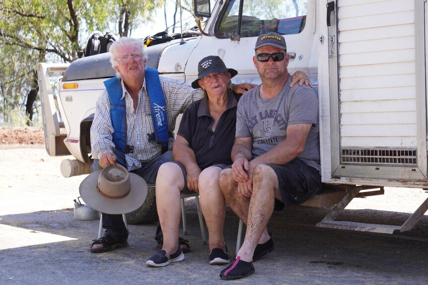 Two men and a woman sitting next to truck