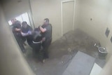 CCTV footage of a man in a black T-shirt in a police cell being put in a headlock by a police officer.