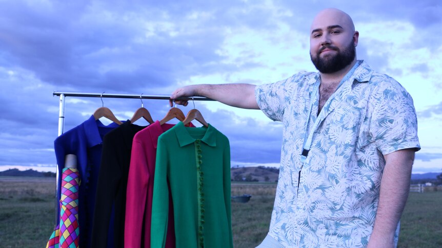 Cameron Robert McCormick standing in a paddock with a garment rack with dresses on it.