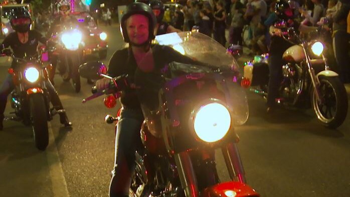A group of women pose ride motorbikes during a night parade.