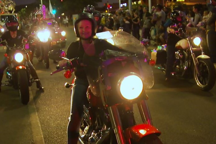 A group of women pose ride motorbikes during a night parade.