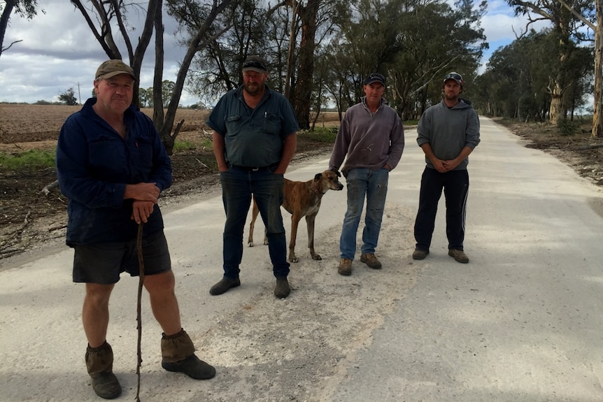 Four men and a dog standing on a dirt road.