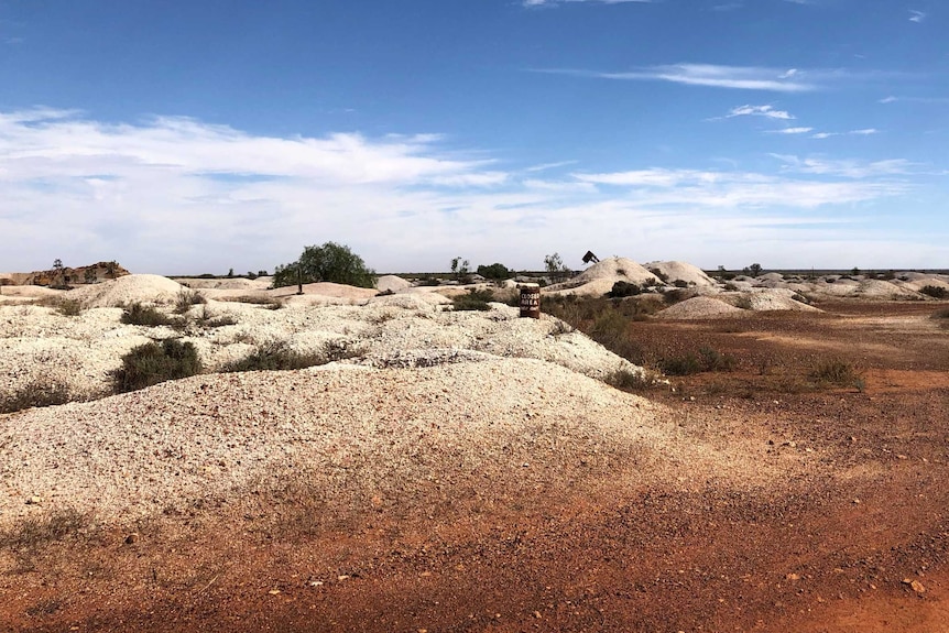 A landscape photo of the White Cliffs opal fields with a clear sky, red earth and white mounds.