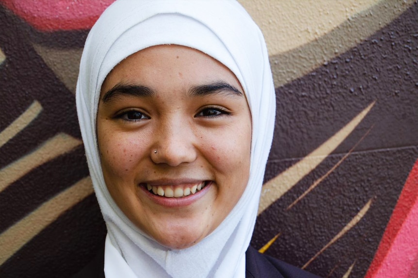 Afghan refugee Rahila Abdul Hadi smiling and standing in front of a mural she made in Toowoomba