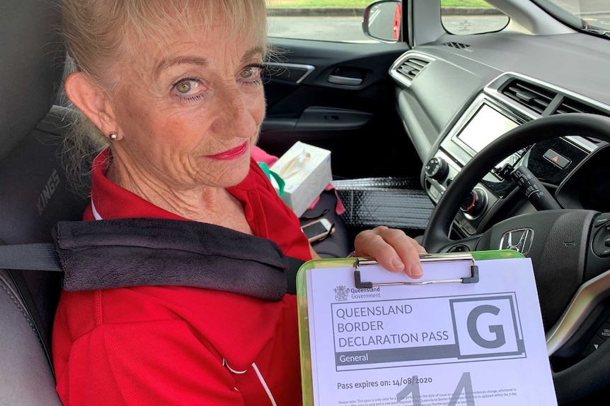 A woman in a car holding up a printed border declaration pass on a clipboard to the camera