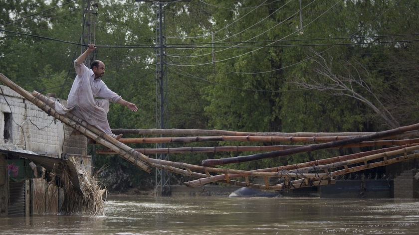A man crosses a makeshift bridge to escape his flooded home in Pakistan's north-west