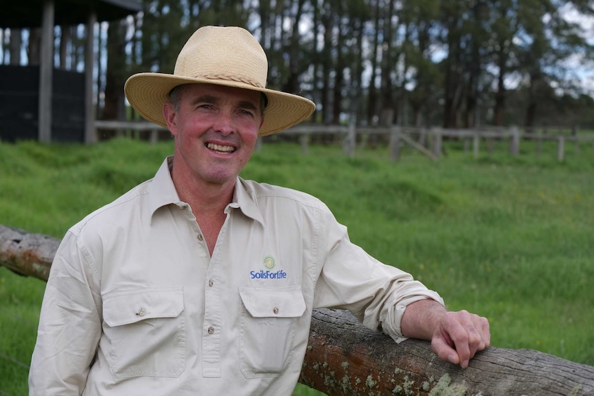 A farmer wearing a hat stands next to a fence