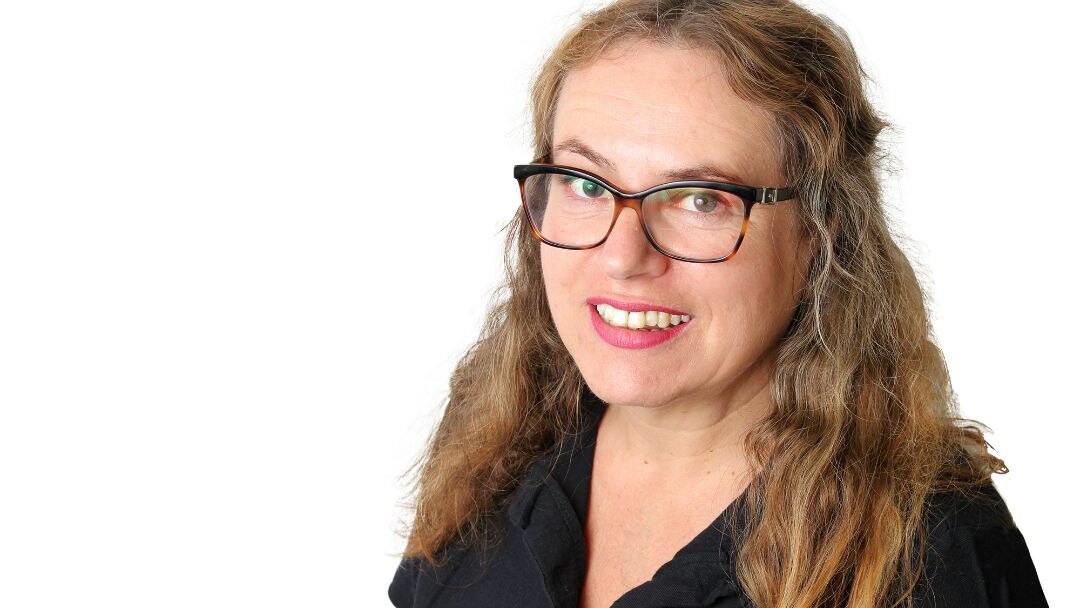 A headshot of a woman with long brown hair and glasses.