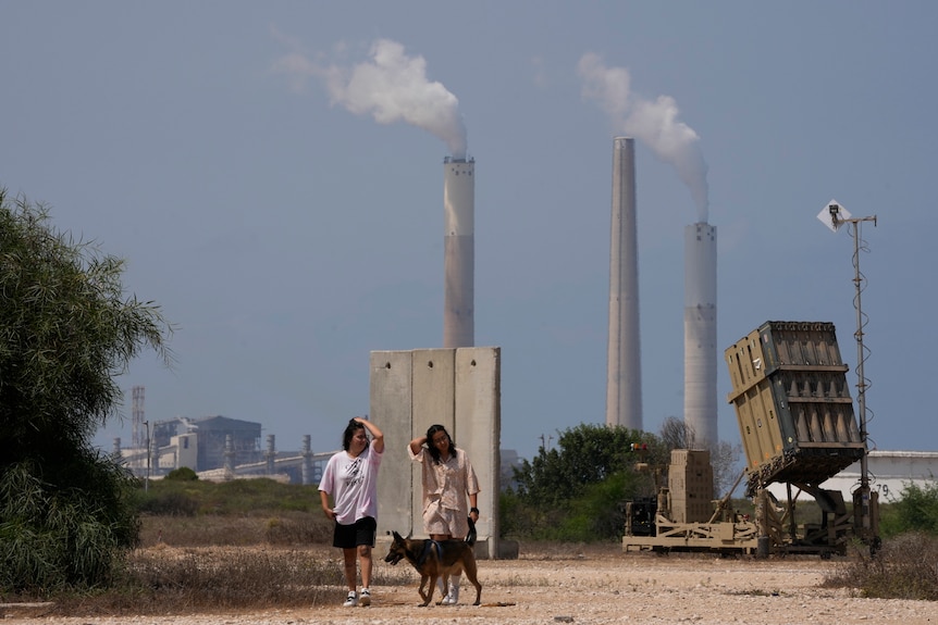 Two people walk their dog past an Iron Dome air defence system.