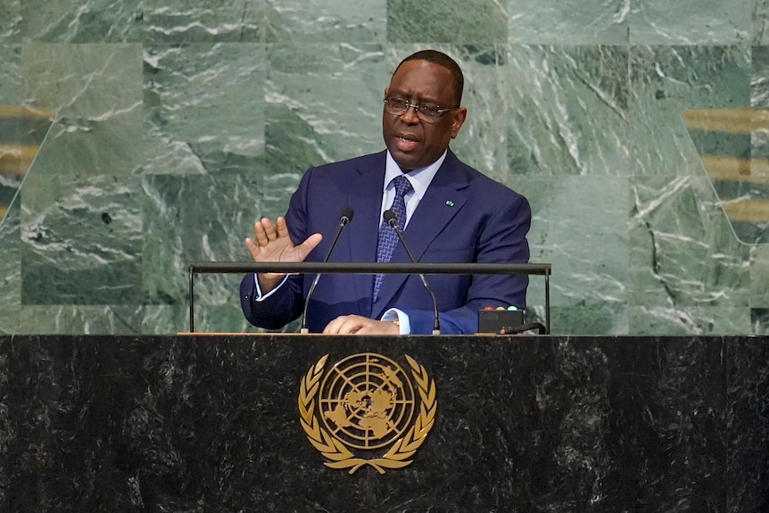 A man standing at a podium, gestures with his right hand as he speaks