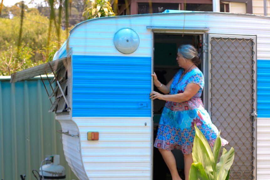 Woman in blue dress standing outside a caravan.