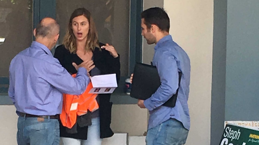 A woman approached by two men with a piece of paper in her hands.